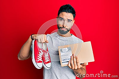 Young man with beard taking casual red shoes from box depressed and worry for distress, crying angry and afraid Stock Photo