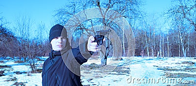 Young man in black clothes shoots with a pistol on nature in winter Stock Photo