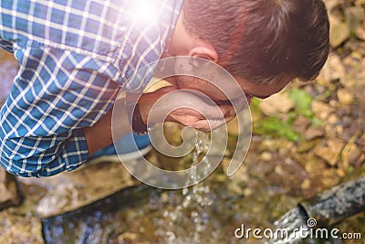 A young man in a blue shirt drinking clean water from an underground source Stock Photo