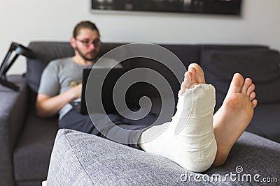 Young man with a broken leg on the sofa Stock Photo