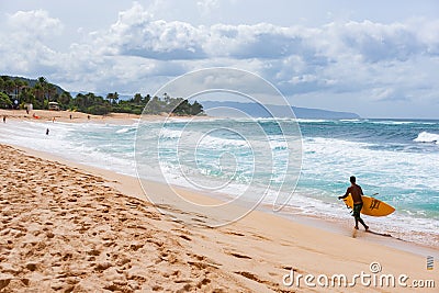 Young man carrying yellow surfboard along beach to go surfing Editorial Stock Photo