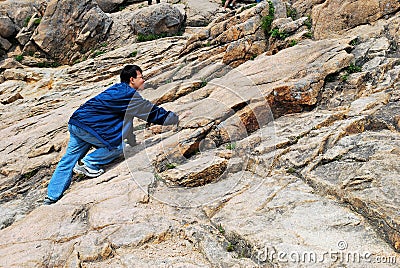 Young man climbing treacherous mountain cliff Stock Photo