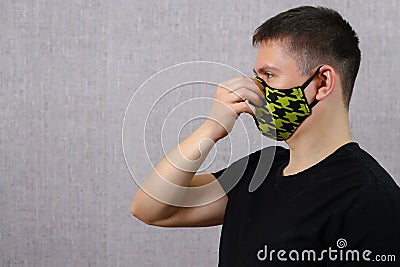 Young man in a cloth mask is turned sideways and holds his hand to his face. protection from coronovirus. covid-19 Stock Photo