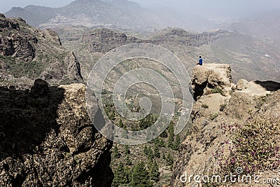 Lonely adventurer on blue t shirt sitting on top of rocky mountain edge Stock Photo