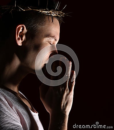 Young man in crown of thorns, martyr with closed eys imploringly clasped his hands side shot Stock Photo