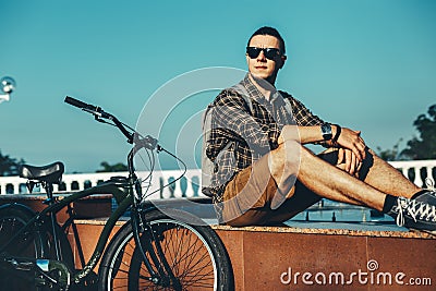 Young Man Cyclist Sitting On Fountain Next To Bicycle In Summer Park Daily Lifestyle Urban Resting Concept Stock Photo