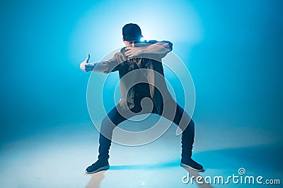 Young man dancer dancing funky hip hop on isolated studio neon blue background Stock Photo