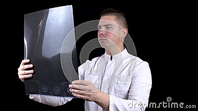 A young man doctor checks the results of an MRI scan of a spine. A man examines an MRI image on a black background. Stock Photo