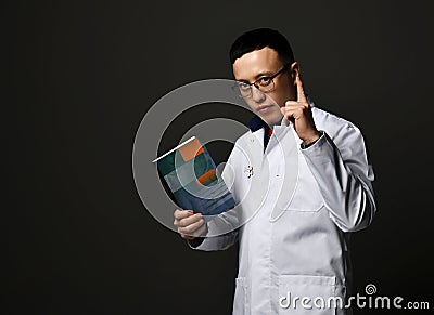 Young man doctors in white medical uniform gown stands holding professional books with blank cover in hand and finger up Stock Photo