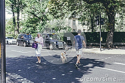 A young man with a dog and a woman crossing Grove End Road in St John's Wood, City of Westminster, London Editorial Stock Photo