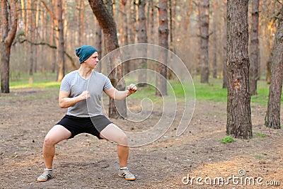 Young man doing workout and squats in morning park. Stock Photo