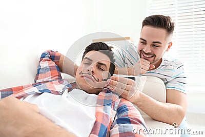 Man drawing mustache on face of sleeping friend indoors. April fool`s day Stock Photo