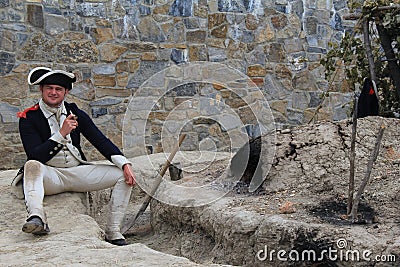 Young man dressed as soldier of 1776,sitting next to fire with pipe,Fort Ticonderoga,New York,2014 Editorial Stock Photo