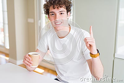 Young man drinking take away cup of coffee at home surprised with an idea or question pointing finger with happy face, number one Stock Photo