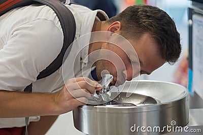 A young man is drinking water from a free fountain at the airport. Stock Photo