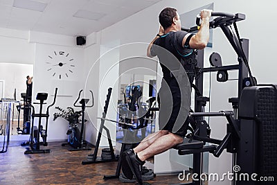 Young man in ems suit pulls up on sports simulator. Strained male athlete trains on gravitron machine in gym or fitness club Stock Photo