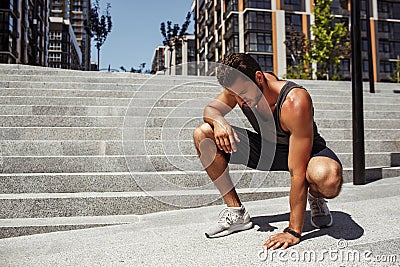 Young man exercising outside. Concentrated serious guy touching asphalt and looks down. Rest after exercising, running Stock Photo