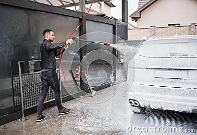 Young man foaming car by gun on car wash station outdoors. Stock Photo