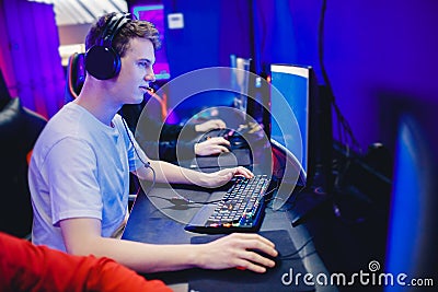 Young man gamer play online video games with headphones in internet club cafe, blue color. Esports concept Stock Photo