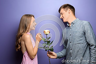 Young man giving beautiful flower to his beloved girlfriend on color background Stock Photo