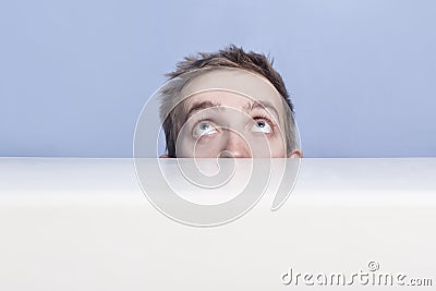 Young man is hiding behind the table. Spying. Voyeurism. Stock Photo