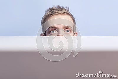 Eyes of young man look out from behind the table. Voyeurism. Stock Photo