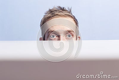 Young man is hiding. Spying. Voyeurism. Eyes look out from behind the table. Stock Photo