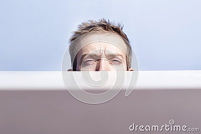 Young man is hiding. Squinted eyes behind the table. Spying. Voyeurism. Stock Photo