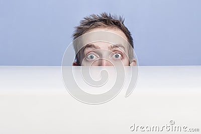 Surprised eyes of young man look out from behind the table. Voyeurism. Stock Photo