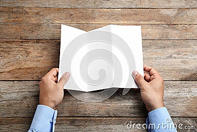 Young man holding blank brochure at table, top view. Mock up for design Stock Photo