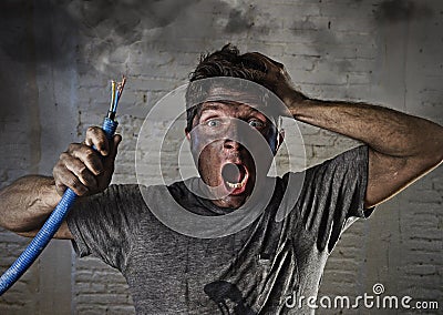 Young man holding cable smoking after electrical accident with dirty burnt face in funny sad expression Stock Photo