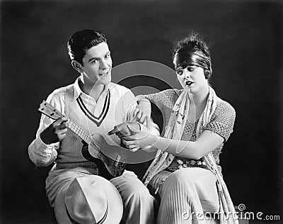 Young man holding a guitar with a young woman teaching him how to play Stock Photo