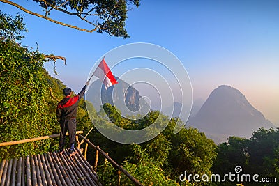 A young man holding Indonesian flag in the mountain peak. Indonesian independence day Stock Photo