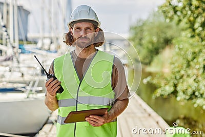 Young man holding radio and looking at camera working in yacht docks Stock Photo