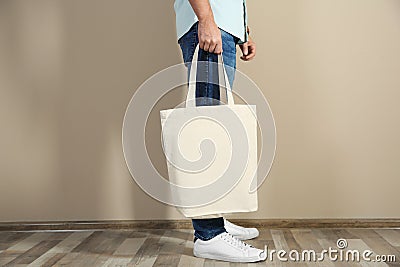 Young man holding textile bag against color wall, closeup. Stock Photo