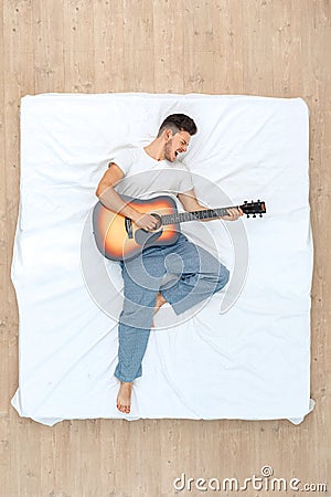 Bedtime. Guy lying on bed top view palying guitar singing excited Stock Photo