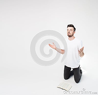 Young man isolated over background. Praying alone on knees in front Bible on floor and look up. Believe in Jesus Christ Stock Photo