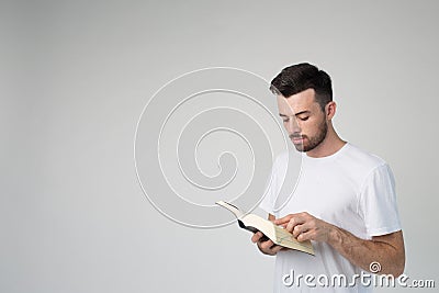 Young man isolated over background. Side view of guy reading book and standing in room alone. Point with finger. Smart Stock Photo