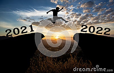 A young man jump between 2021 and 2022 years over the sun and through on the gap of hill silhouette evening colorful sky. happy n Stock Photo