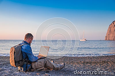 Young man with laptop working on the beach. Freedom, remote work, freelancer, technology, internet, travel and vacation concepts Stock Photo