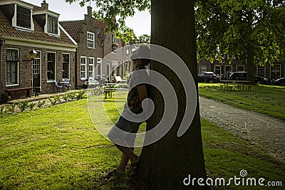 Young man leaning on his back in a tree, resting. Park in residential area with typical dutch houses. Stock Photo