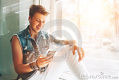 Young man listen music with headphones and smartphone sitting on windowsill Stock Photo