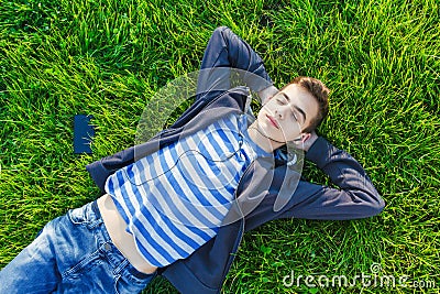 Young man listening music from smart phone on the grass in the park. Stock Photo