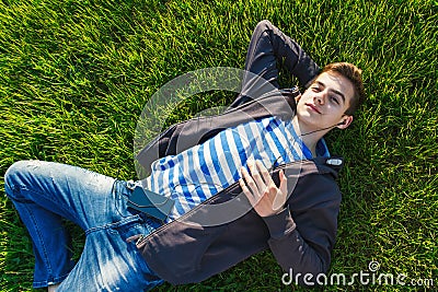 Young man listening music from smart phone on the grass in the park. Stock Photo