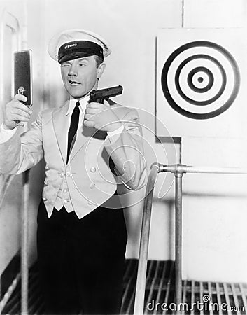 Young man looking at a mirror and aiming at a dartboard with a handgun Stock Photo