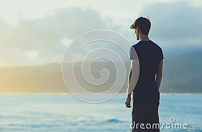 A young man watching the sunset on the beach alone. Stock Photo