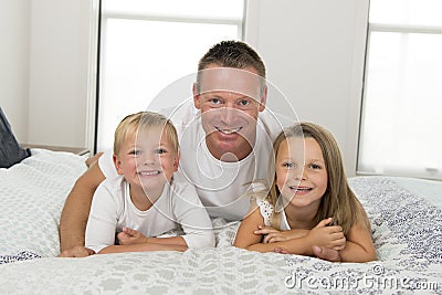 Young man lying on bed together with her little sweet 3 and 7 years old son and daughter playing happy in family father children l Stock Photo