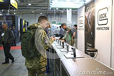 Young man in military uniform standing in front of the stand with pistols Glock presented and looking at them Editorial Stock Photo