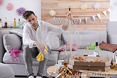 Young man with mop suffering from hangover in room after party Stock Photo