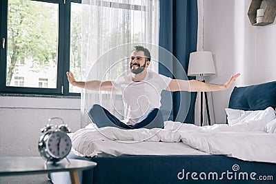 Young man in pajamas stretching while sitting on bed at morning Stock Photo